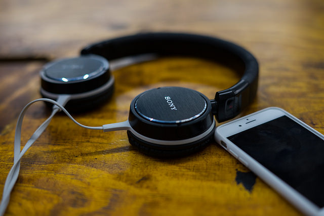 Photograph of black headphones lying flat on a wooden surface, close to a smartphone.