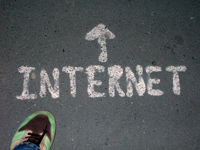 Photograph of the word "Internet" painted on a road in white paint. The photographer's green running shoe can be seen in the lower left corner. An arrow is painted on the ground, showing what direction to follow.